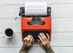 disembodied hands typing on a typewriter with a cup of coffee on the side
