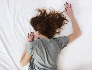 woman lying prone on bed with white sheets