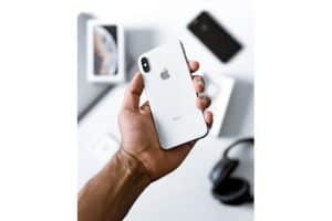 hand holding an iPhone X in the foreground with various gadgets in the background