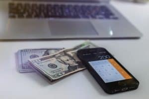 money and phone in the foreground with laptop in the background